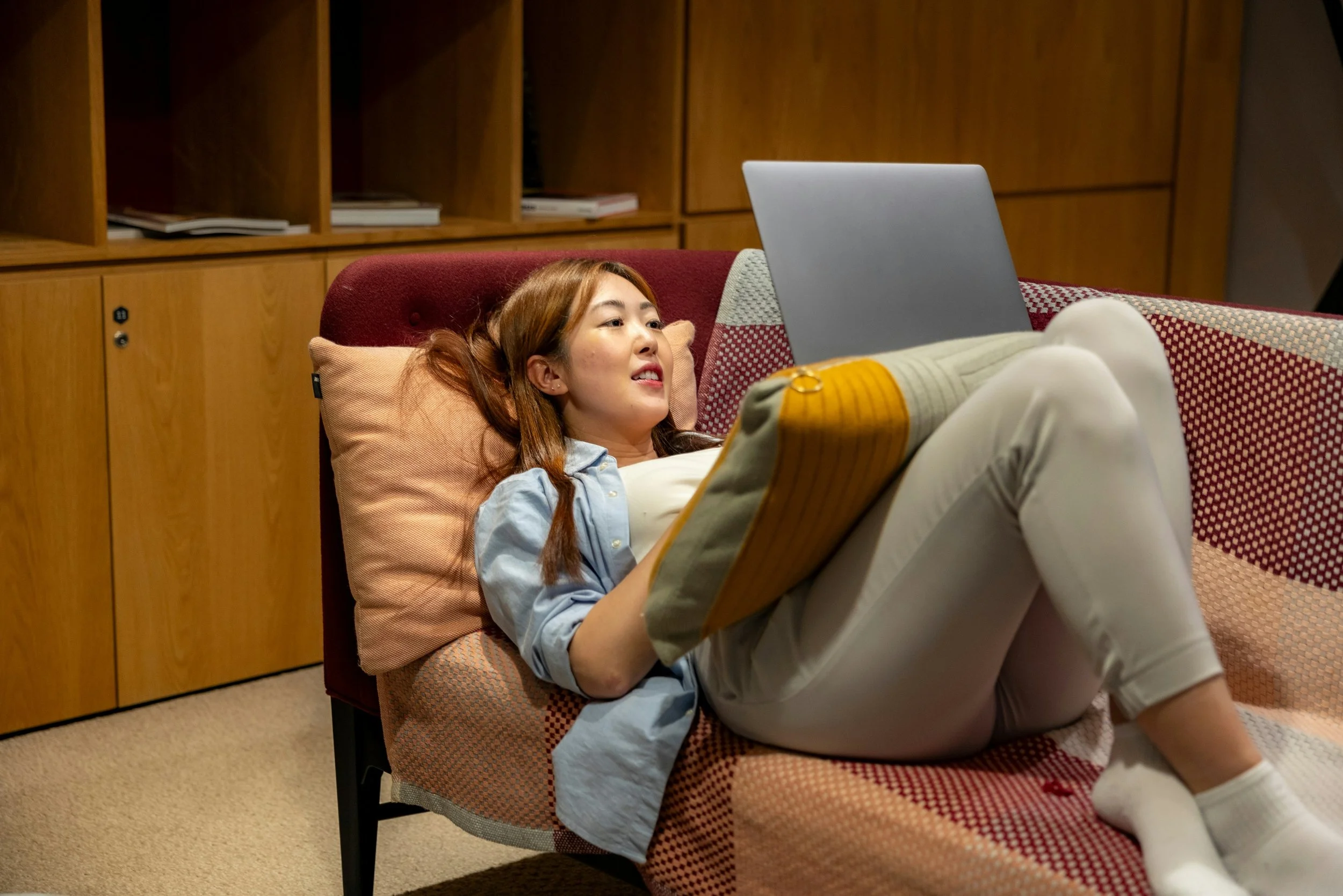 Young woman laying down comfortably on a couch with a laptop in her lap