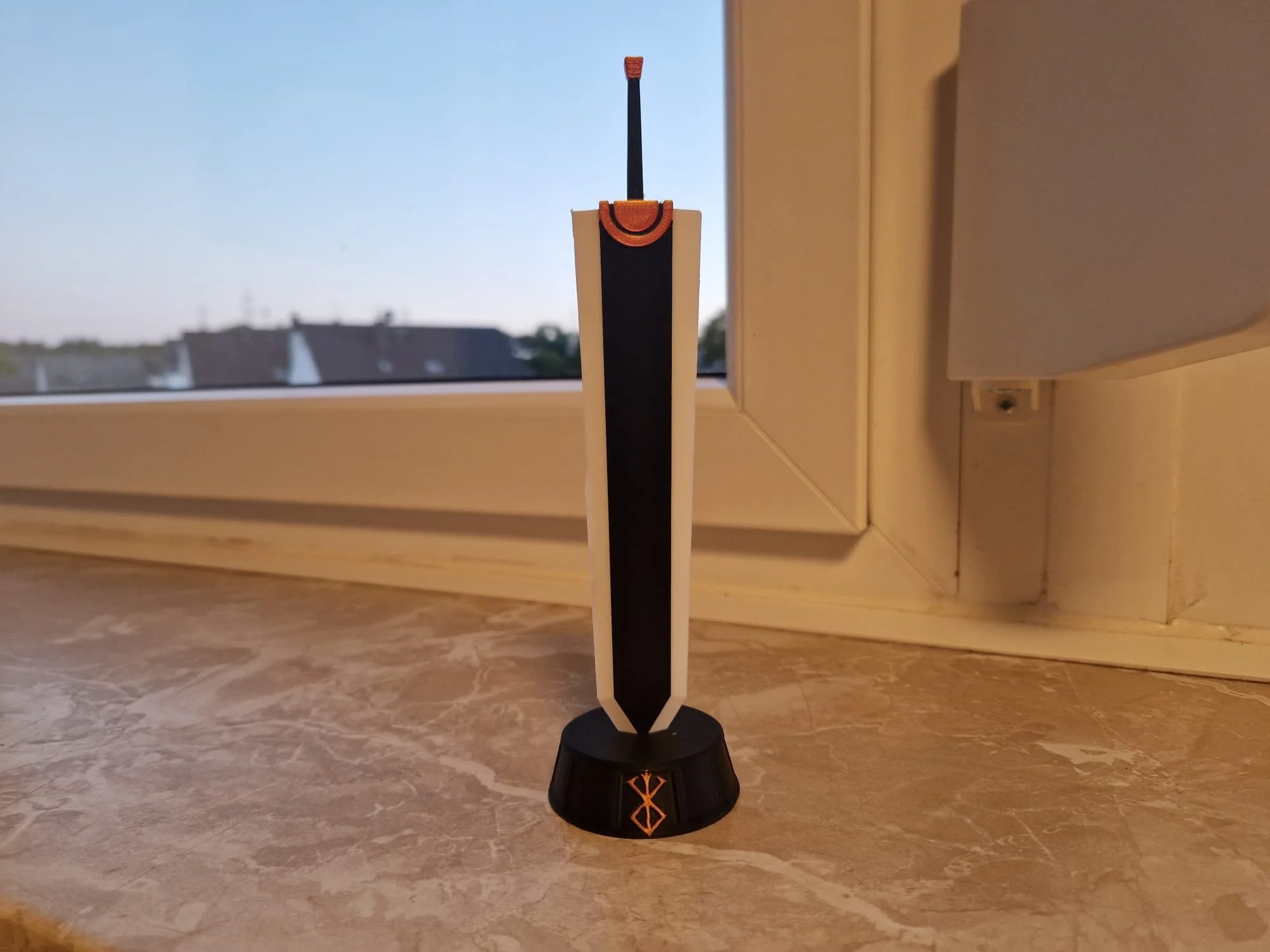 3D-gedrucktes Dragonslayer-Schwert von Guts aus dem Berserk Manga und Anime. Dieses Schwert steckt senkrecht in einem schwarzen 3D-gedruckten Sockel mit orangefarbenem Brand des Opfers. Die Drucke sind mehrfarbig. 