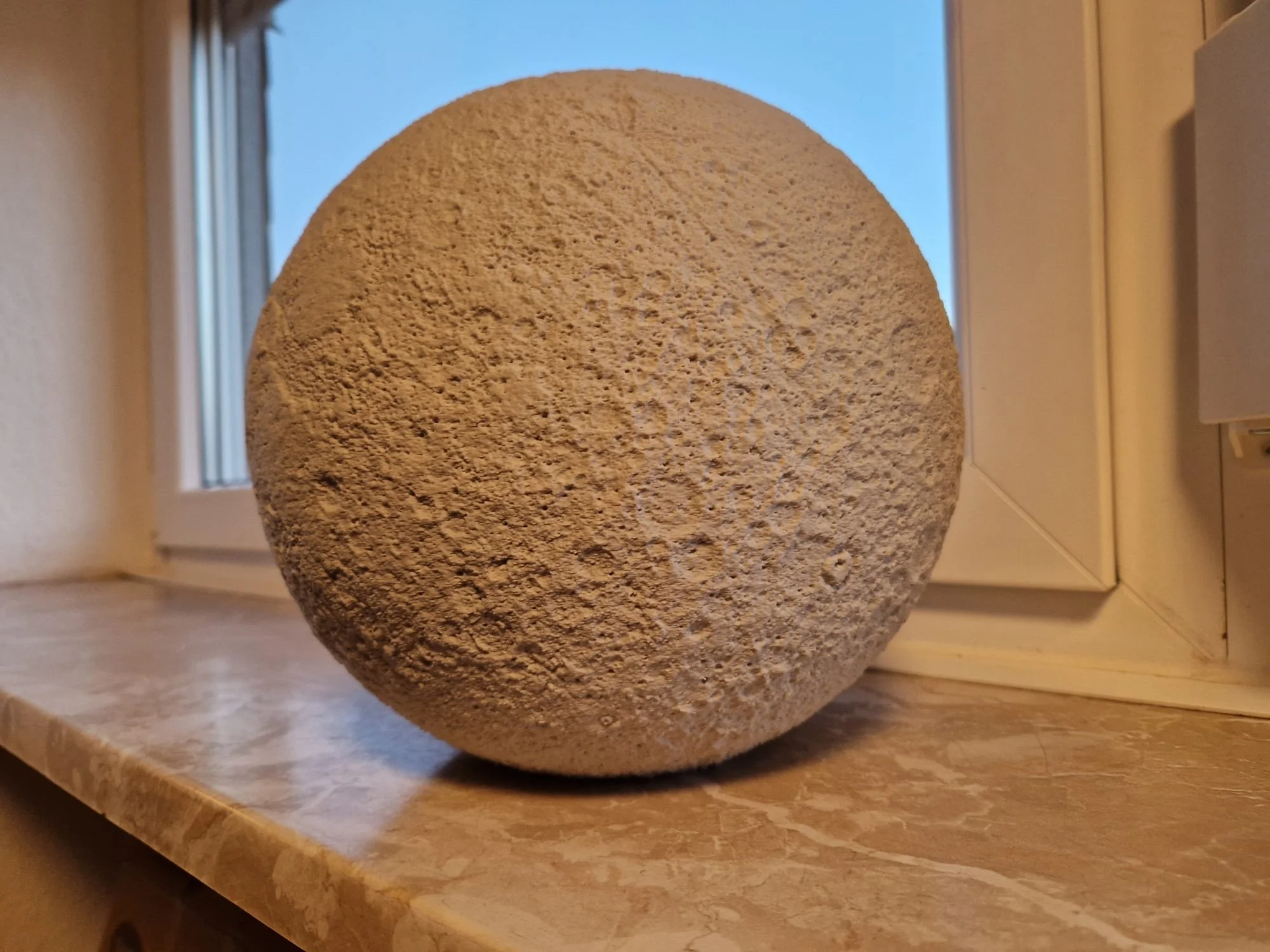 Ein 3D-gedruckter Mond in hellgrauer Farbe. Der Druck ist circa 25 cm groß.