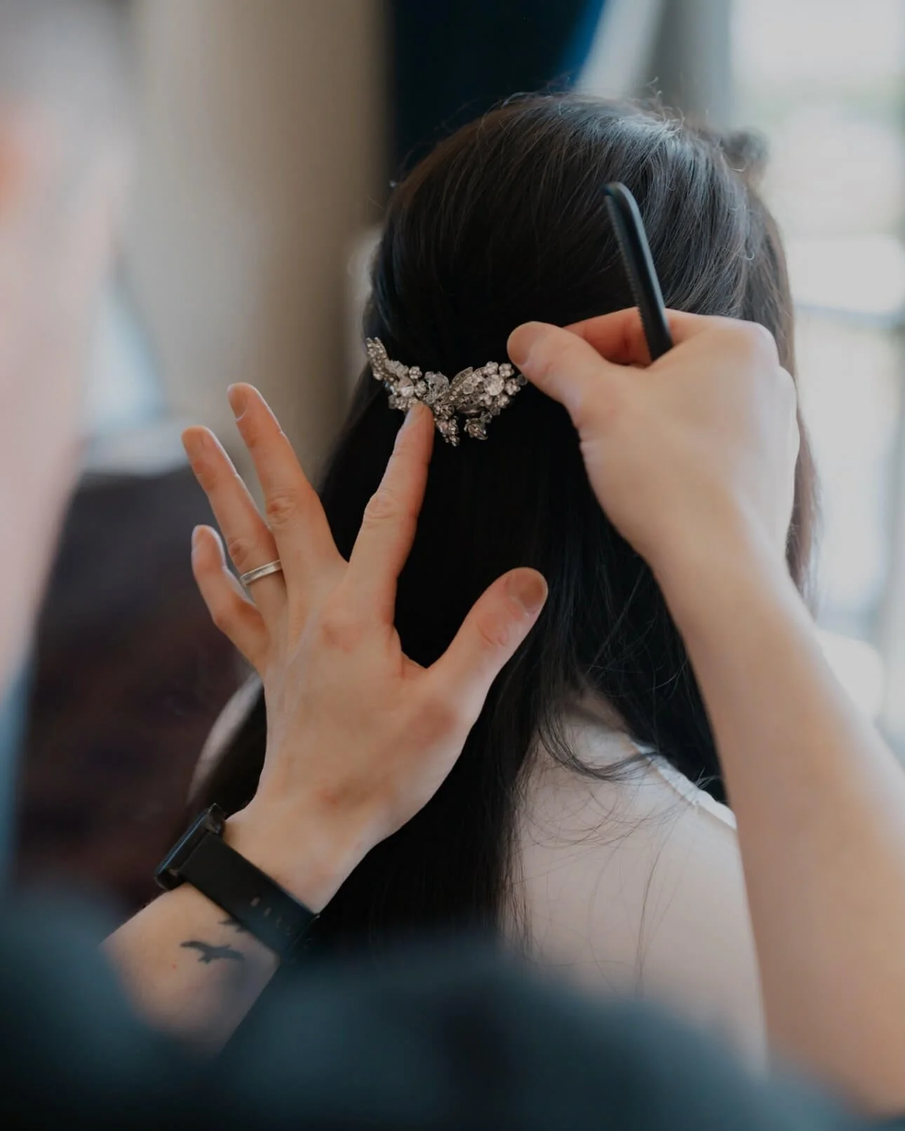 A young woman with long, wavy, brown hair and fair skin looking at the camera, standing in front of two mirrors in a well-lit room.