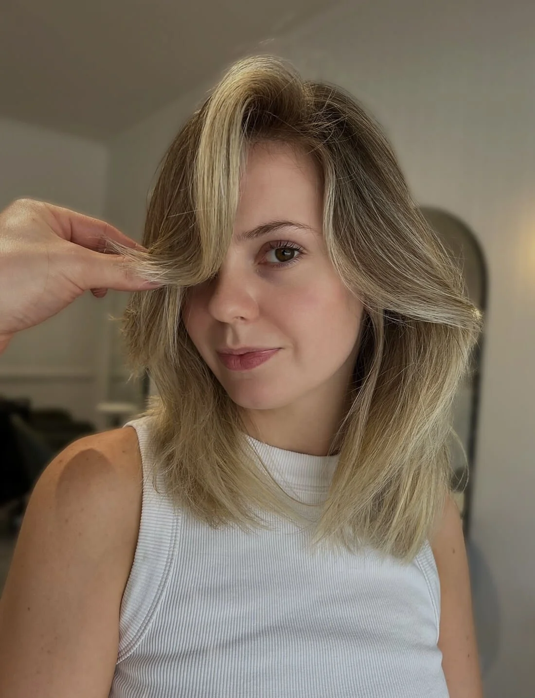 A woman with blonde hair holding a section of her hair with her hand.