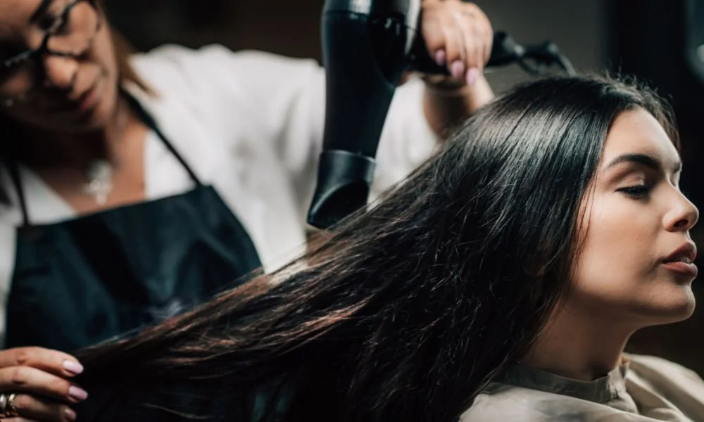 Hair stylist blow drying long straight hair in salon