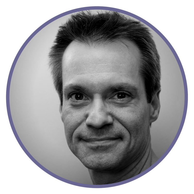 Black and white close-up portrait of a smiling man with short hair, looking at the camera.
