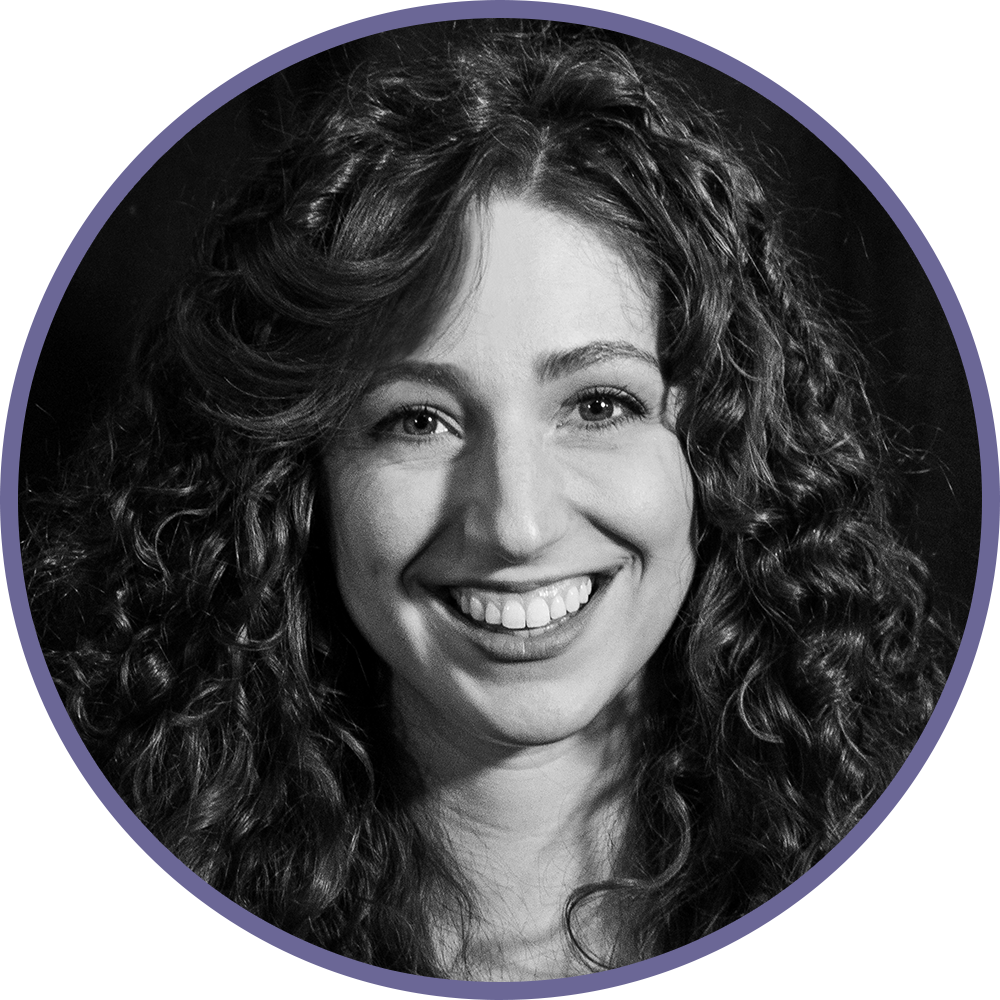 Black and white portrait of a smiling woman with curly hair, looking at the camera.