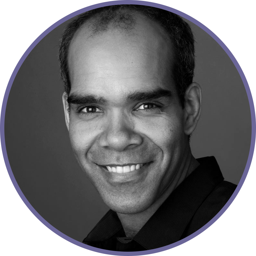 Black and white headshot of a smiling man with dark hair, wearing a dark collared shirt, against a plain gray background.