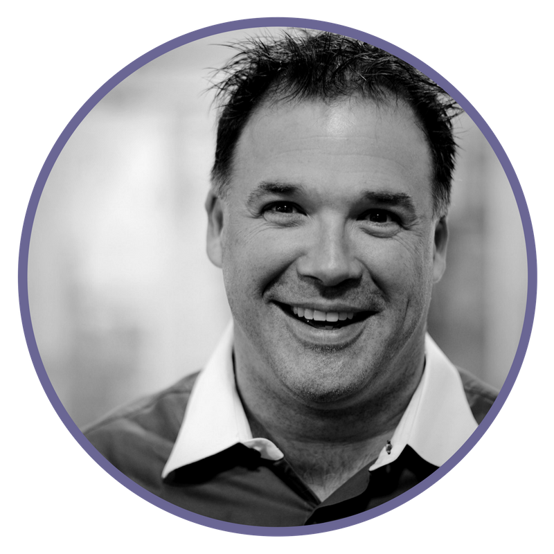 A black and white close-up photograph of a smiling man with short, spiked hair, wearing a collared shirt.