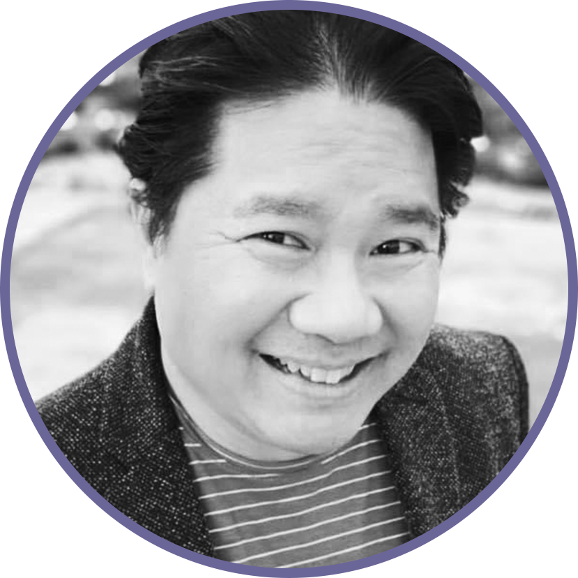 Black and white close-up photo of a smiling Asian man with dark hair, wearing a striped shirt and a textured blazer, outdoors.
