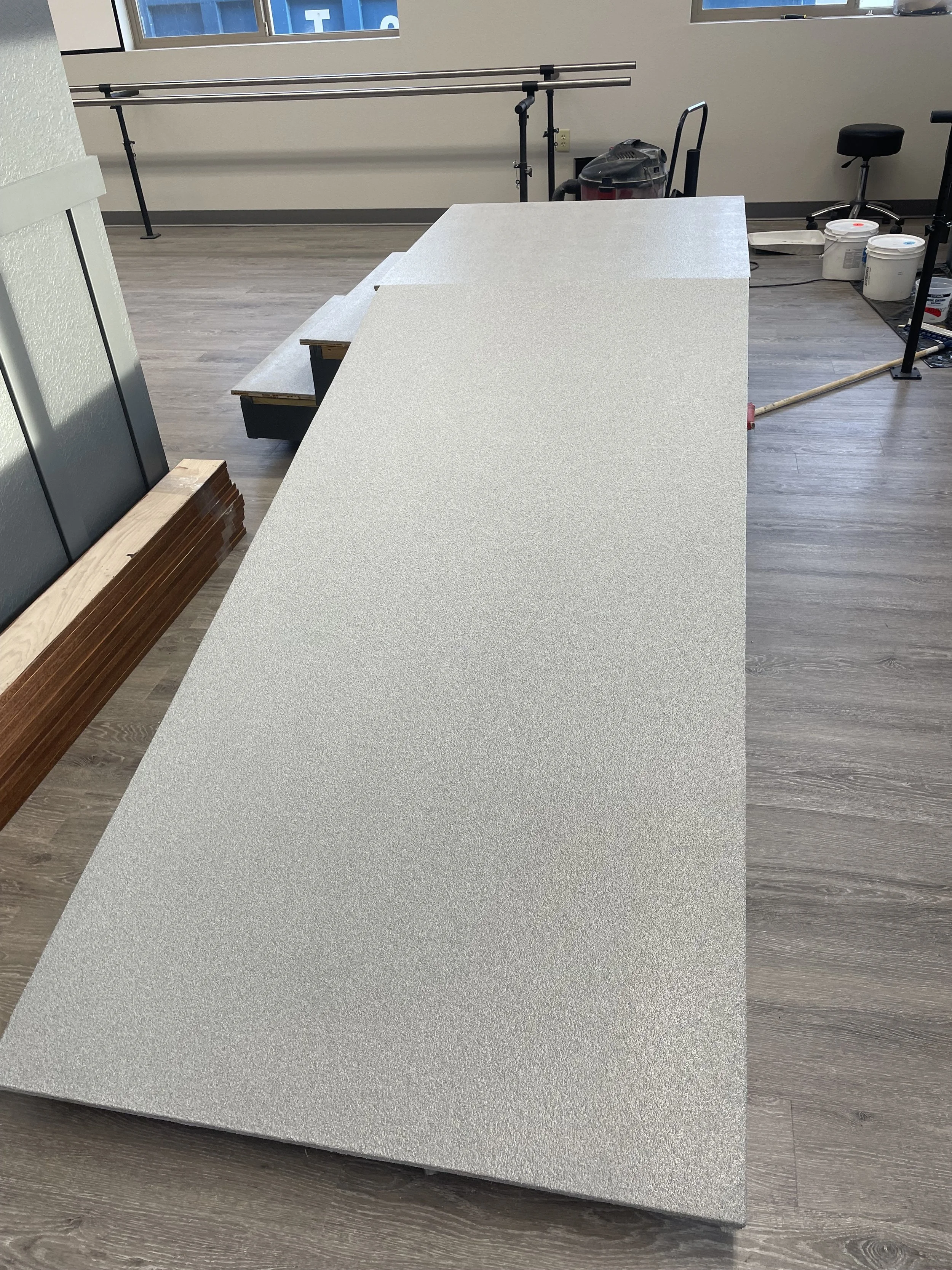 A long, light-colored countertop in an indoor space, with construction tools and materials nearby, and a wall-mounted ballet barre in the background.