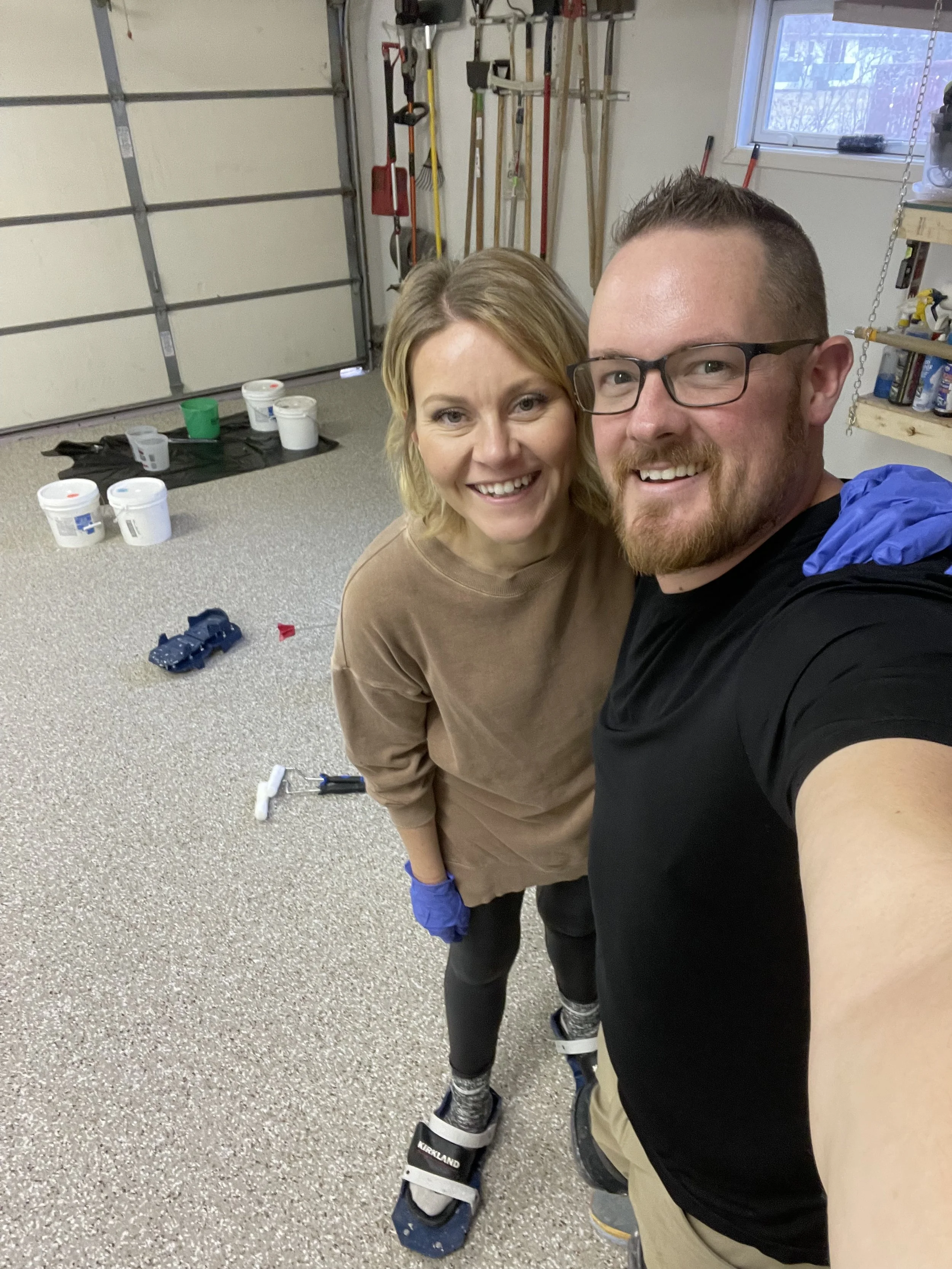 Jesse and Katie owners of Patriot Performance Coatings smiling for a selfie in a garage workshop