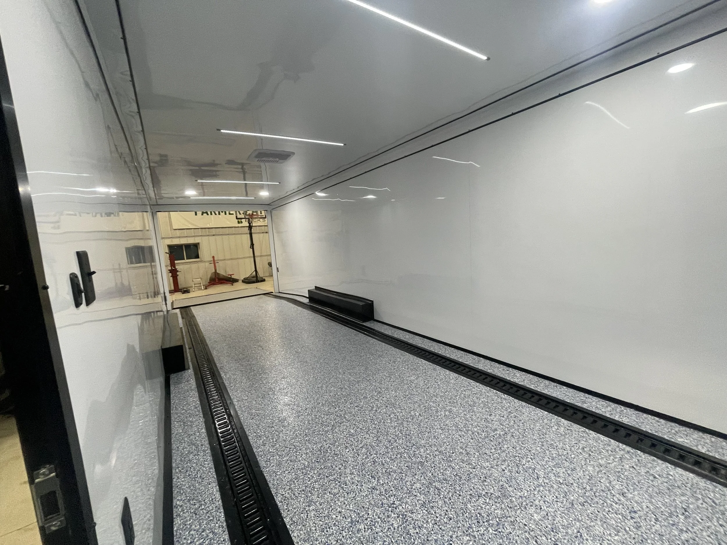 Interior of a clean, empty truck or trailer with white walls and a speckled floor, showing drainage tracks on the floor.