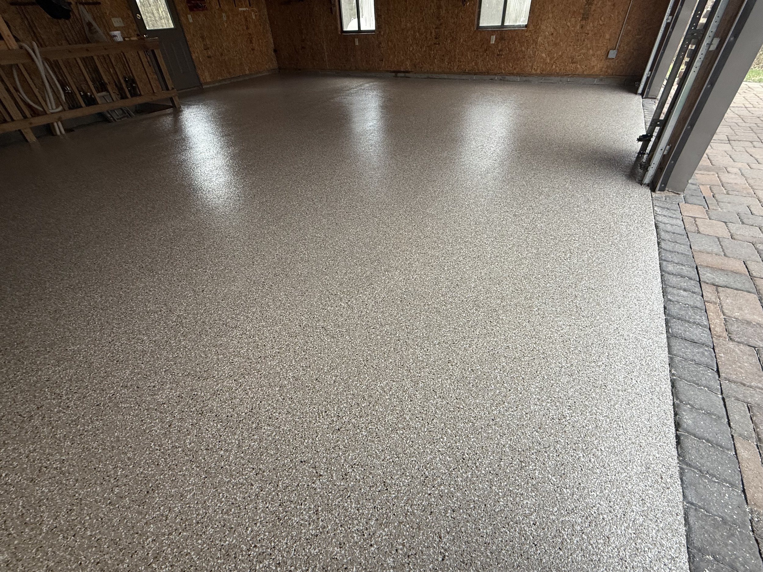 Clean, textured epoxy garage floor with barn wood walls and an open garage door showing a brick driveway outside.