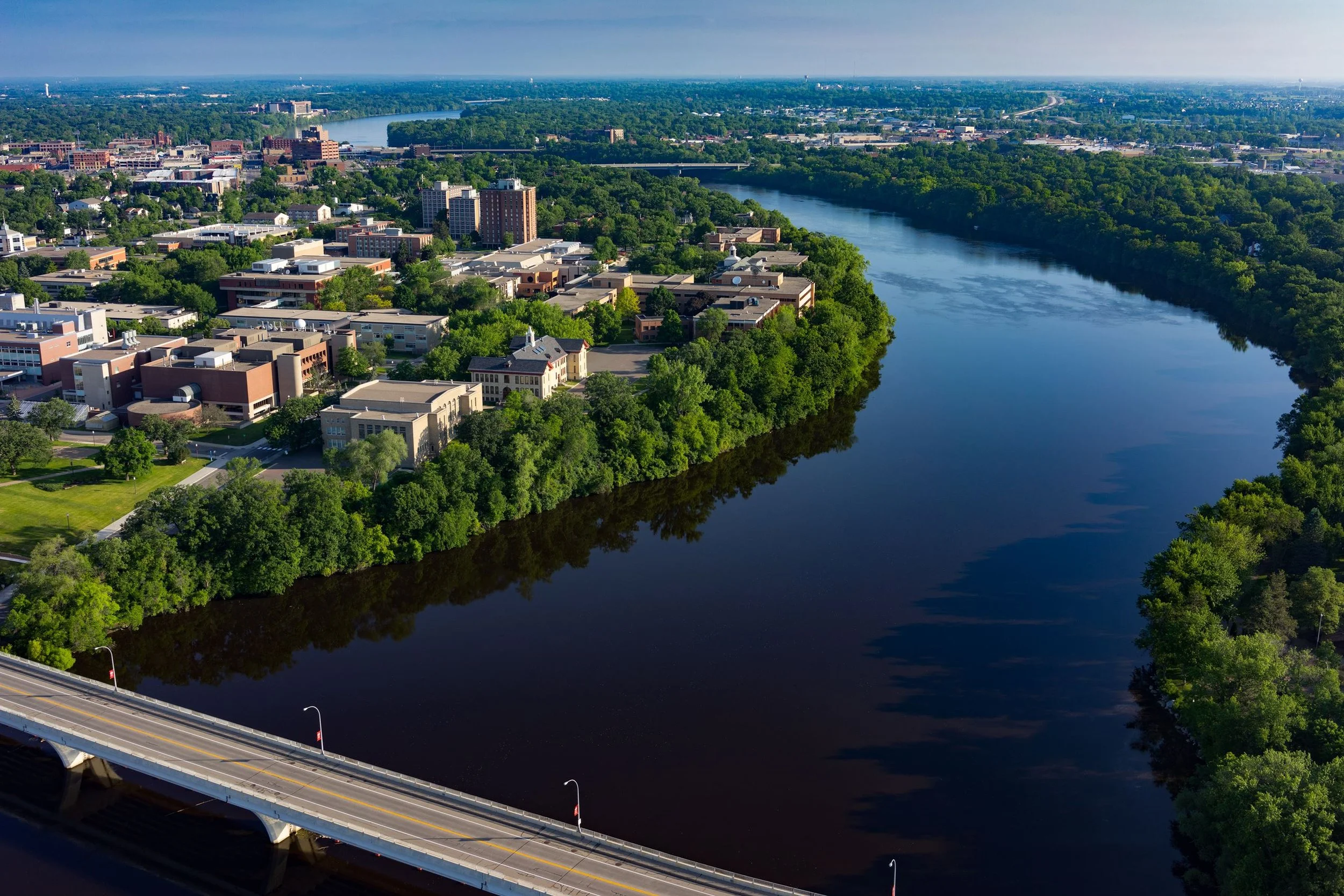 Aerial view of a river running through a city with bridges, surrounded by green trees and buildings.