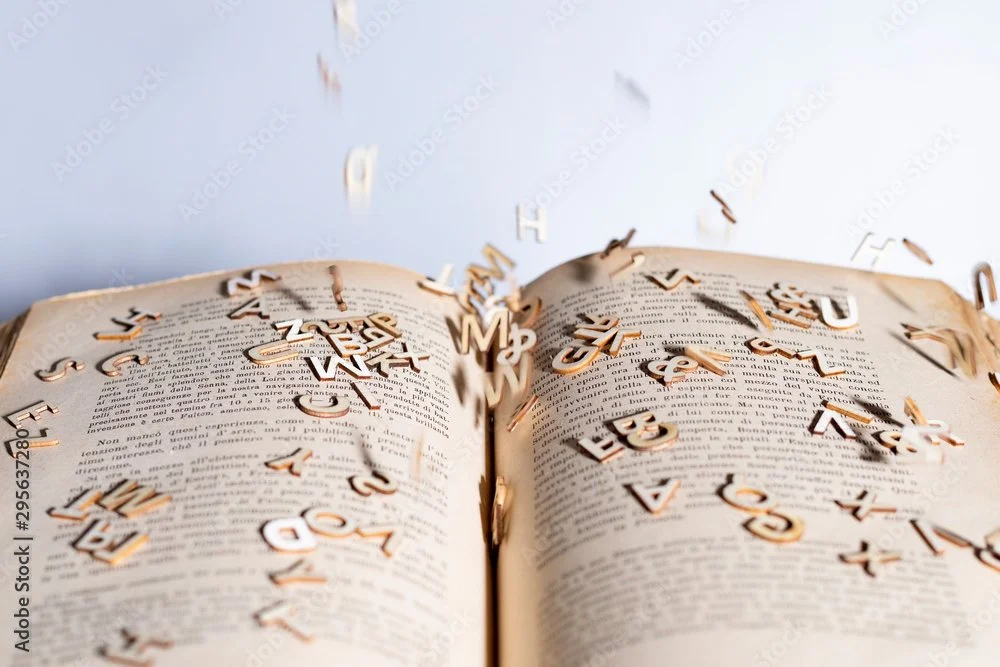 An open book with scattered wooden letters appearing to fly out of the pages.