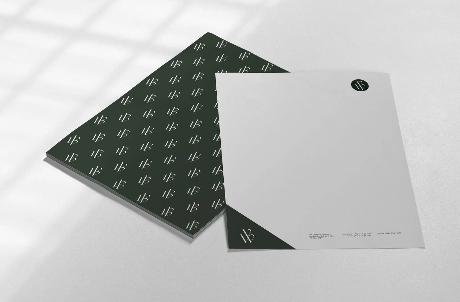 White and black stationery papers with a logo and printed contact information, placed on a white surface.