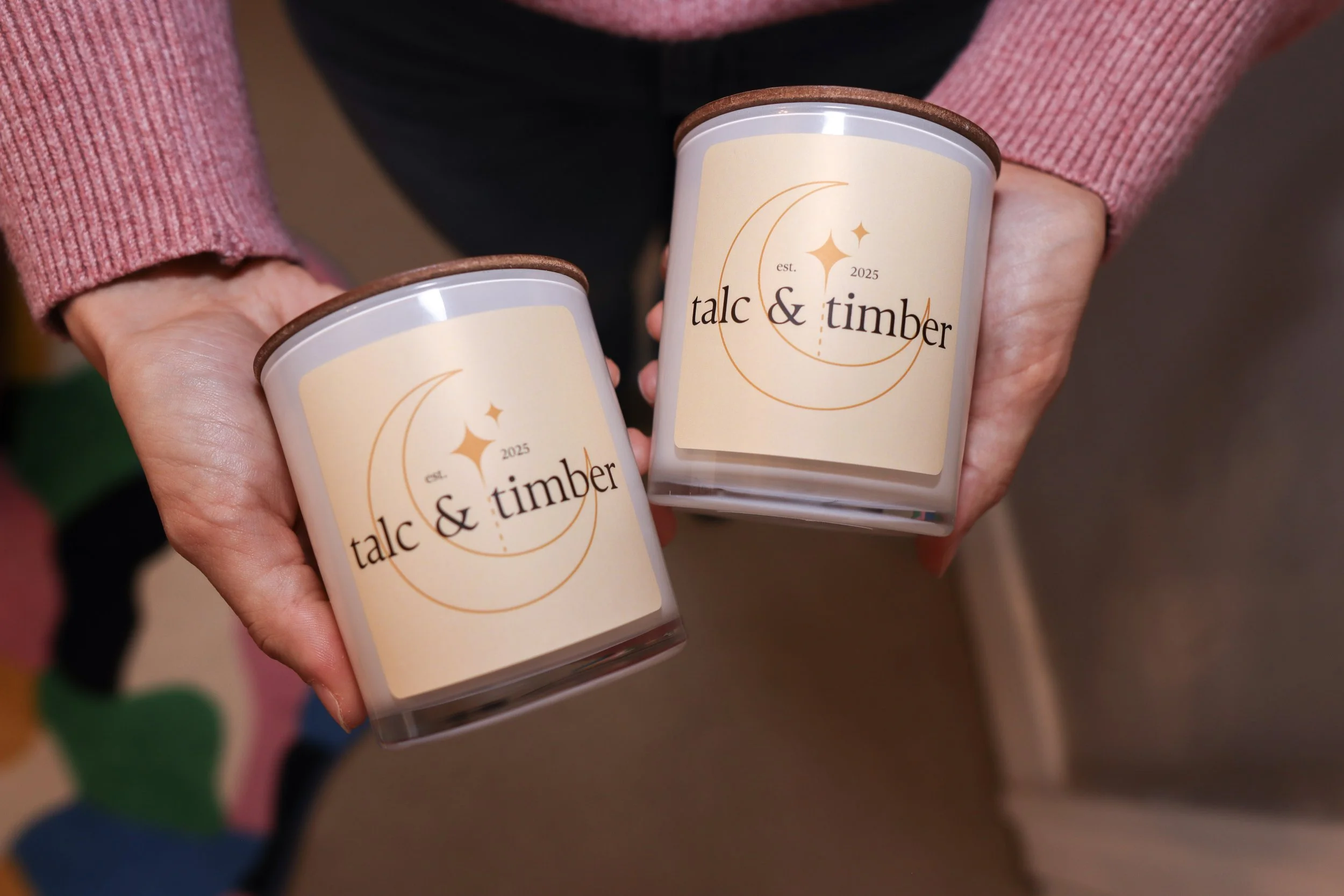 Two hands holding candles with a label that reads "talc & timber," featuring a moon and star design.
