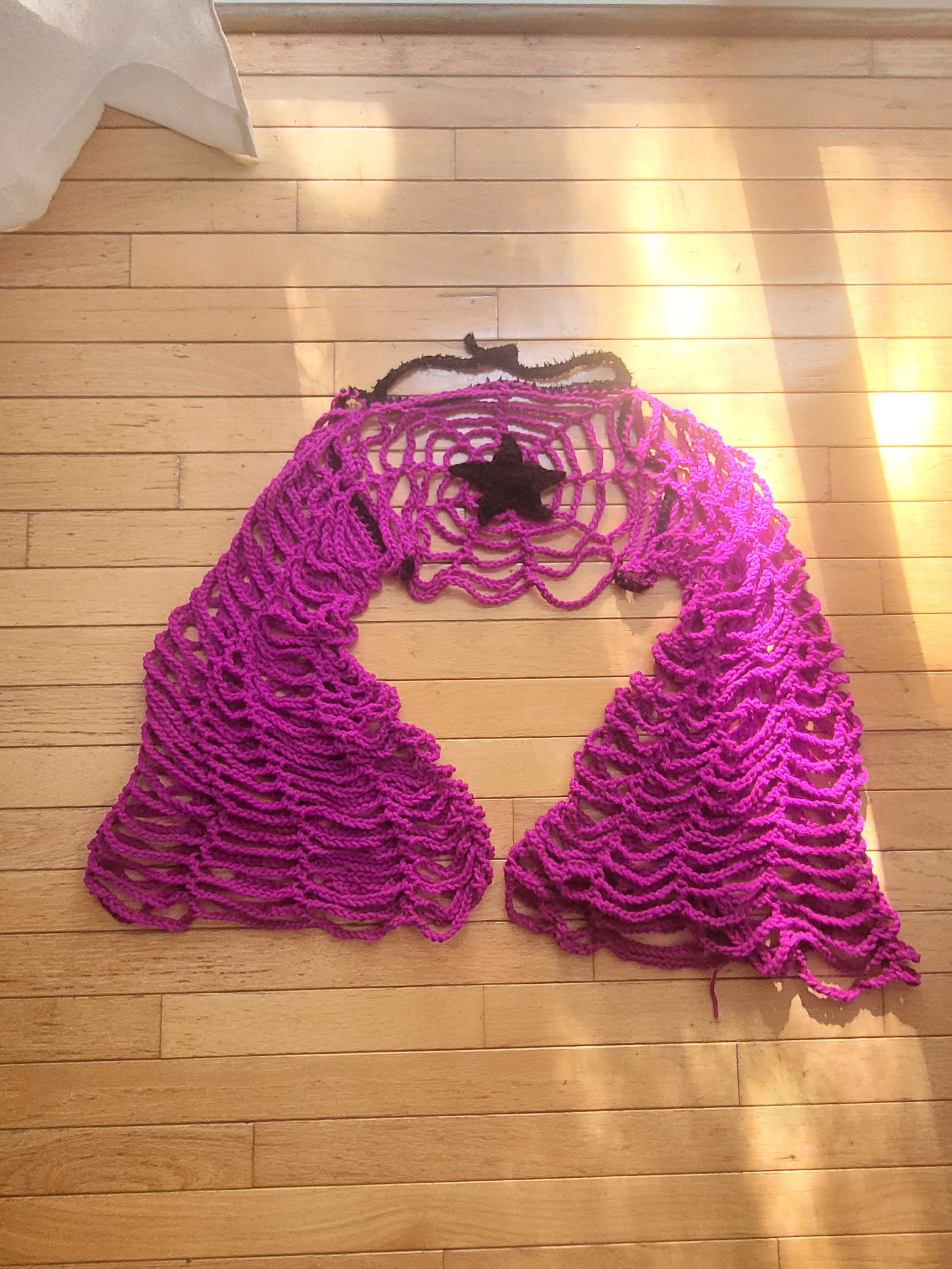 Pink crocheted Halloween decoration with a spider web pattern and black star accents on a wooden floor.