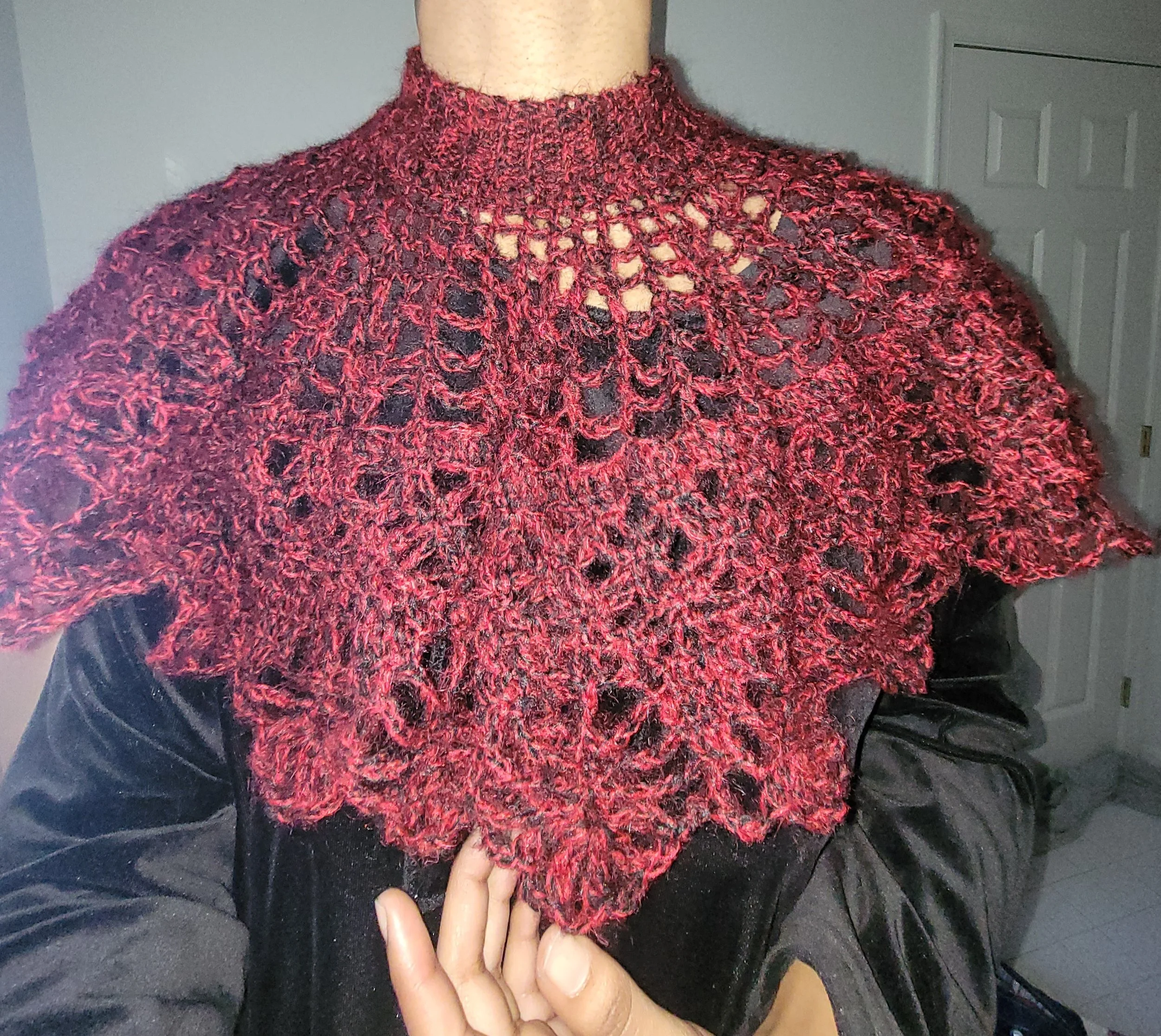 A close-up of a person wearing a red and black crocheted shawl with intricate lace patterns, draped over their shoulders and chest.