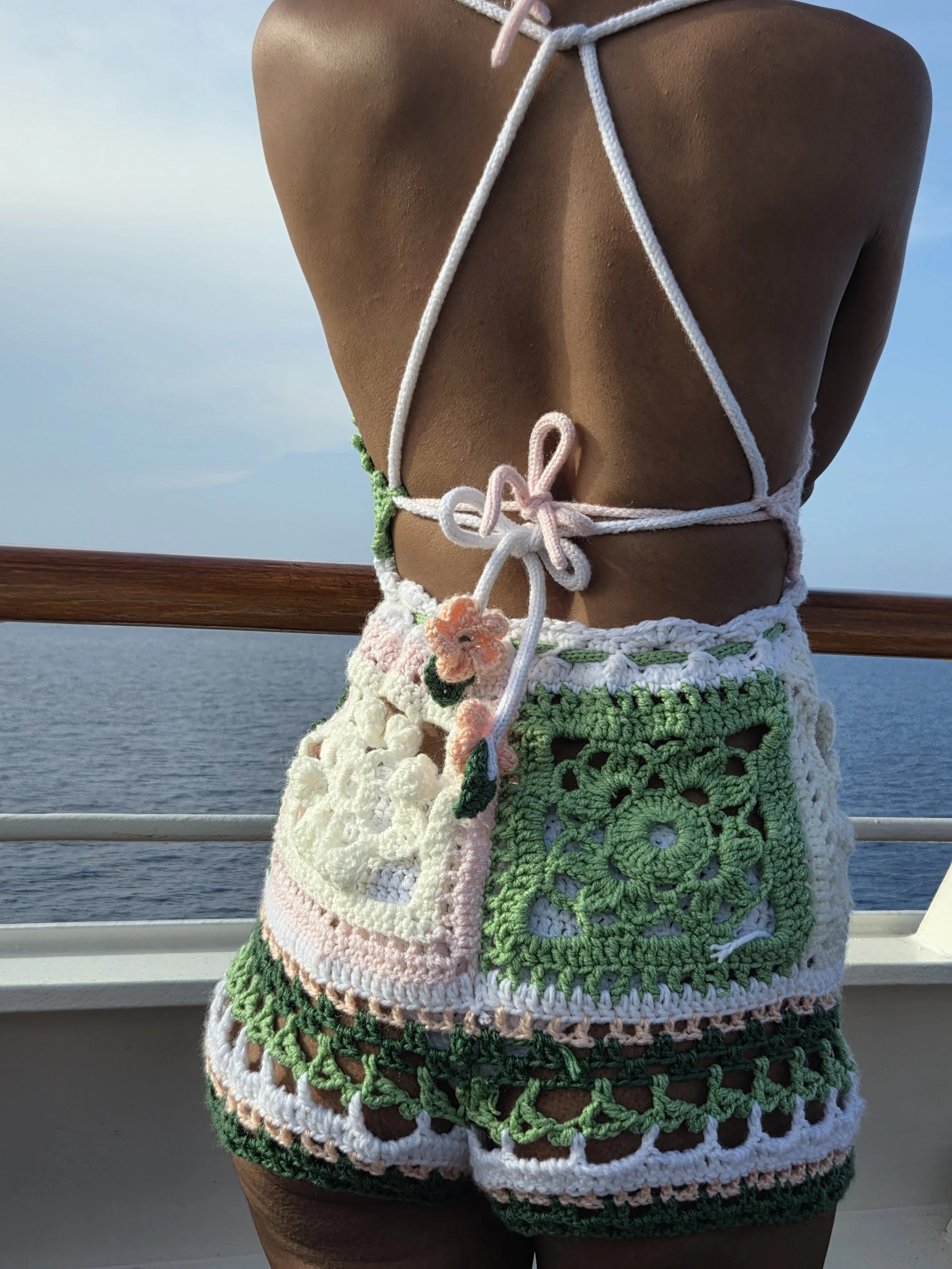Close-up of a woman wearing crochet top and shorts on a boat, with the ocean and sky in the background.