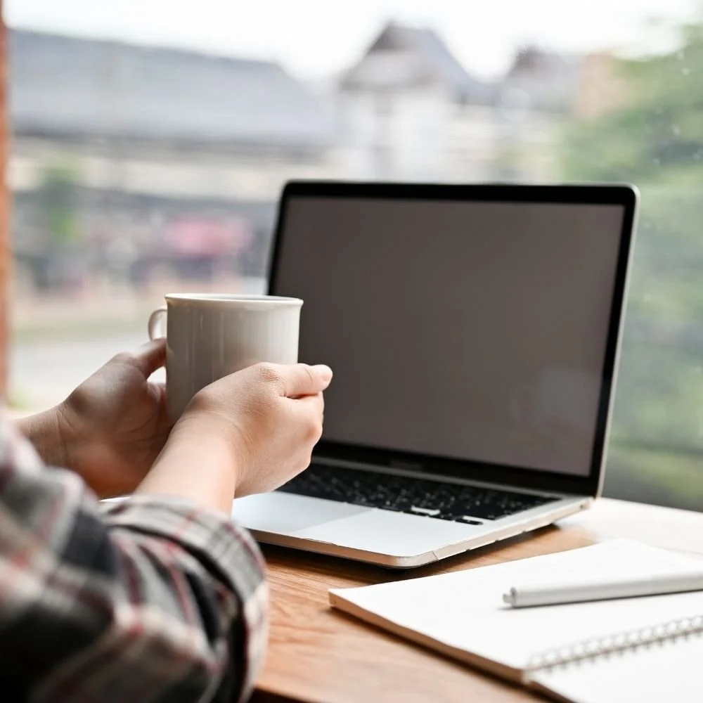 Uma pessoa segurando uma xícara em frente a um laptop