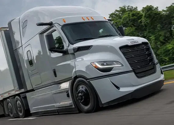 A white semi-truck driving on the highway with green trees in the background.