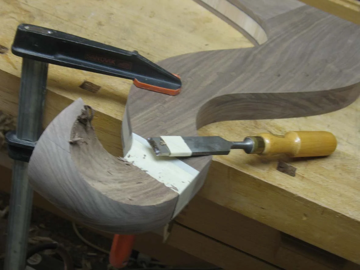 Woodworking project in progress with a carved wooden piece, a chisel, and clamps on a workbench.