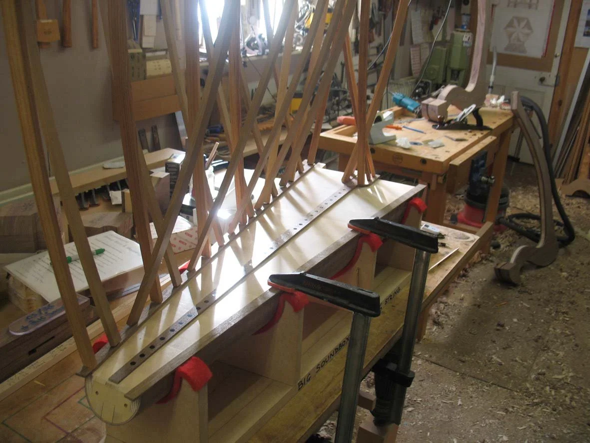 Woodworking workshop with a structure in progress, multiple clamps holding pieces of wood, workbenches with tools.