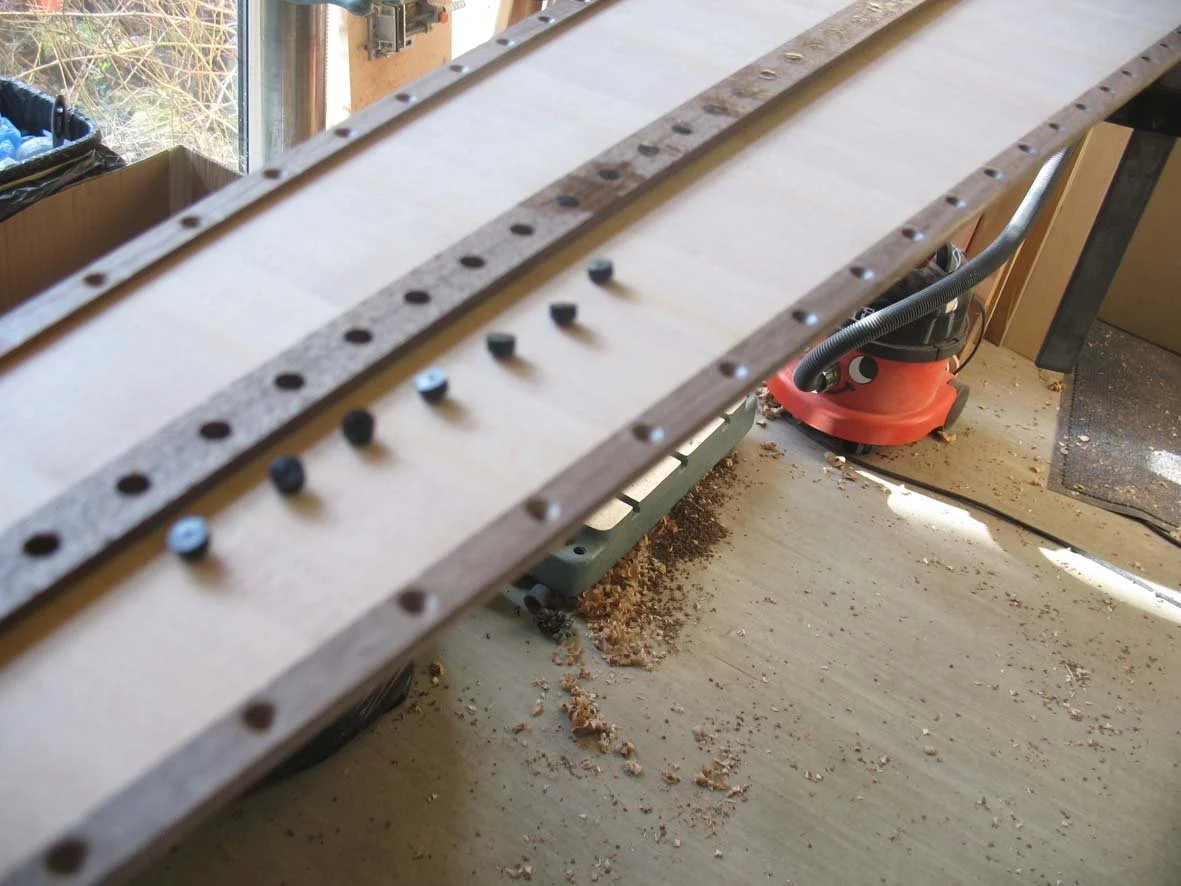 Woodworking workspace with a curved piece of wood clamped on a worktable, dust and wood shavings on the floor.