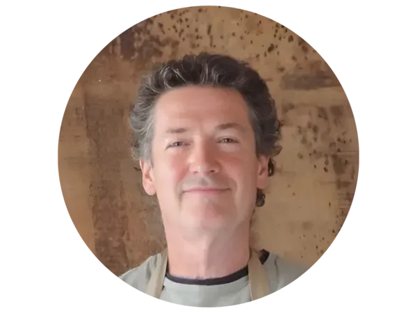 A middle-aged man with curly dark hair smiling in front of a wooden background.