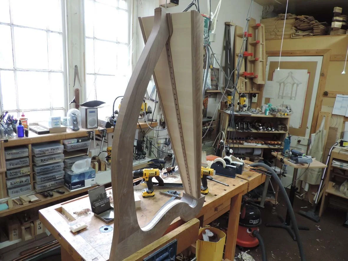 Woodwork project in a workshop with tools and workbenches, featuring a large piece of carved light wood for a harp.