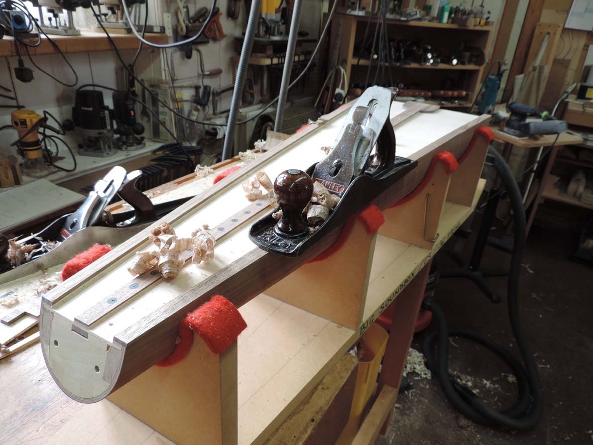 A woodworking workbench surrounded by woodworking tools and shavings, in a busy workshop.