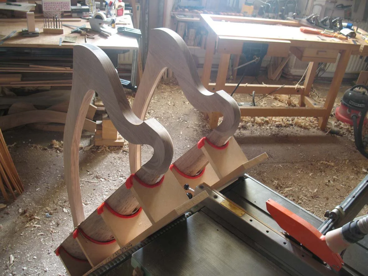 Three curved wooden harp frames clamped to a workbench in a woodworking shop.