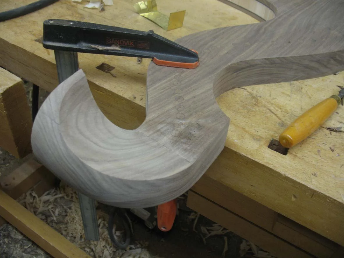 Wooden harp piece being shaped or carved with clamps and woodworking tools on a workbench.