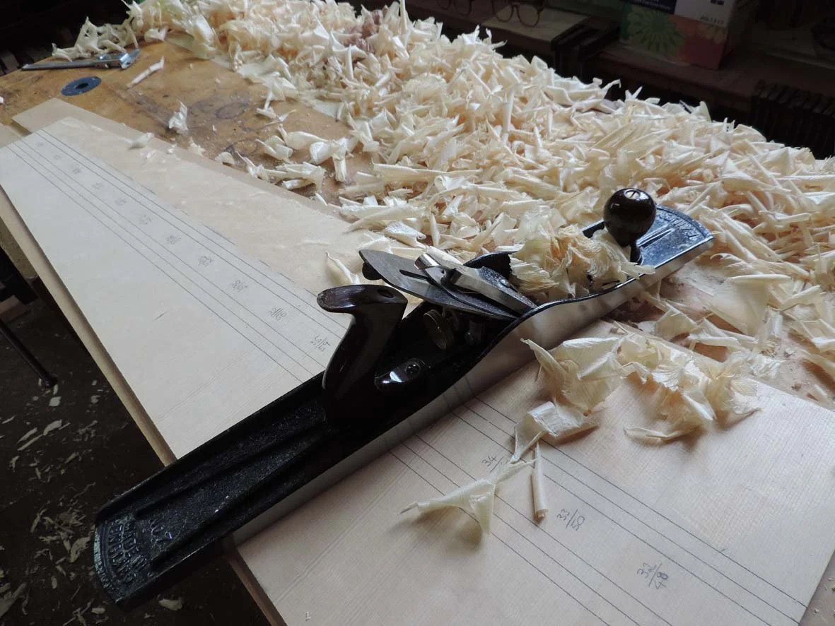 A woodworking plane tool on a wooden workbench surrounded by wood shavings.