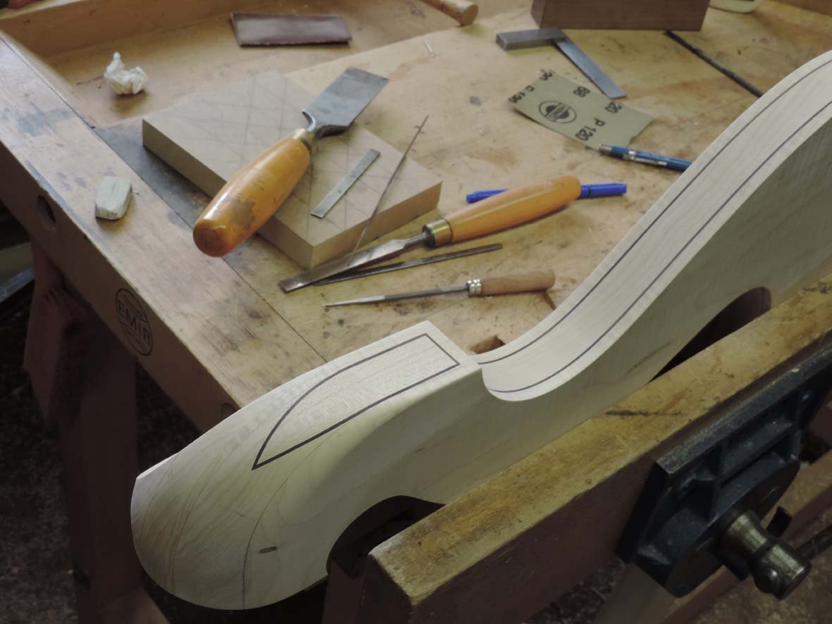 Woodworking workshop with a curved wooden piece, carving tools, chisels, and a square on the workbench.