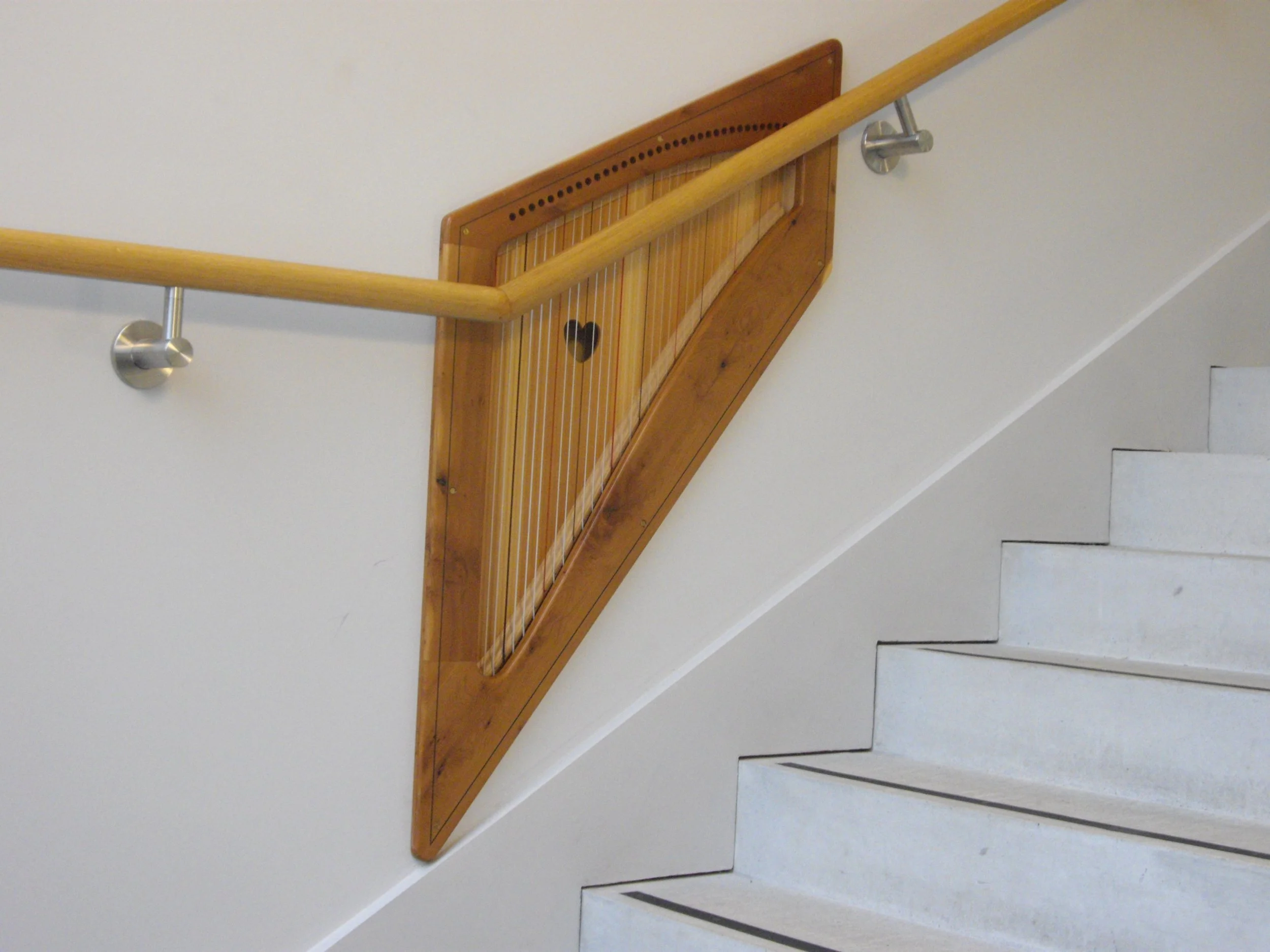 Bespoke harp design on a a staircase with wooden handrail.