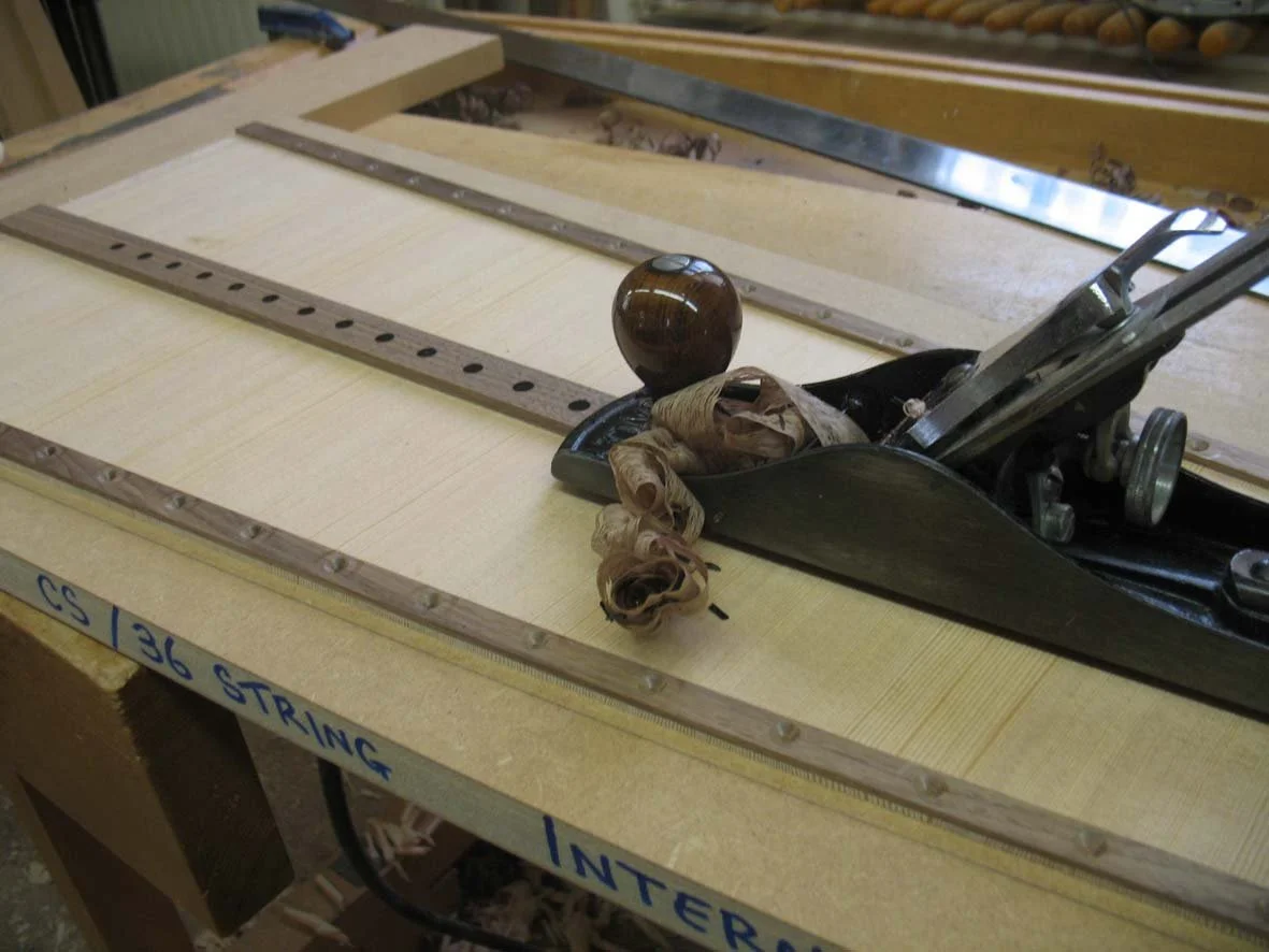 A woodworking plane tool resting on a wooden workbench, with some wood shavings next to it, in a workshop setting.