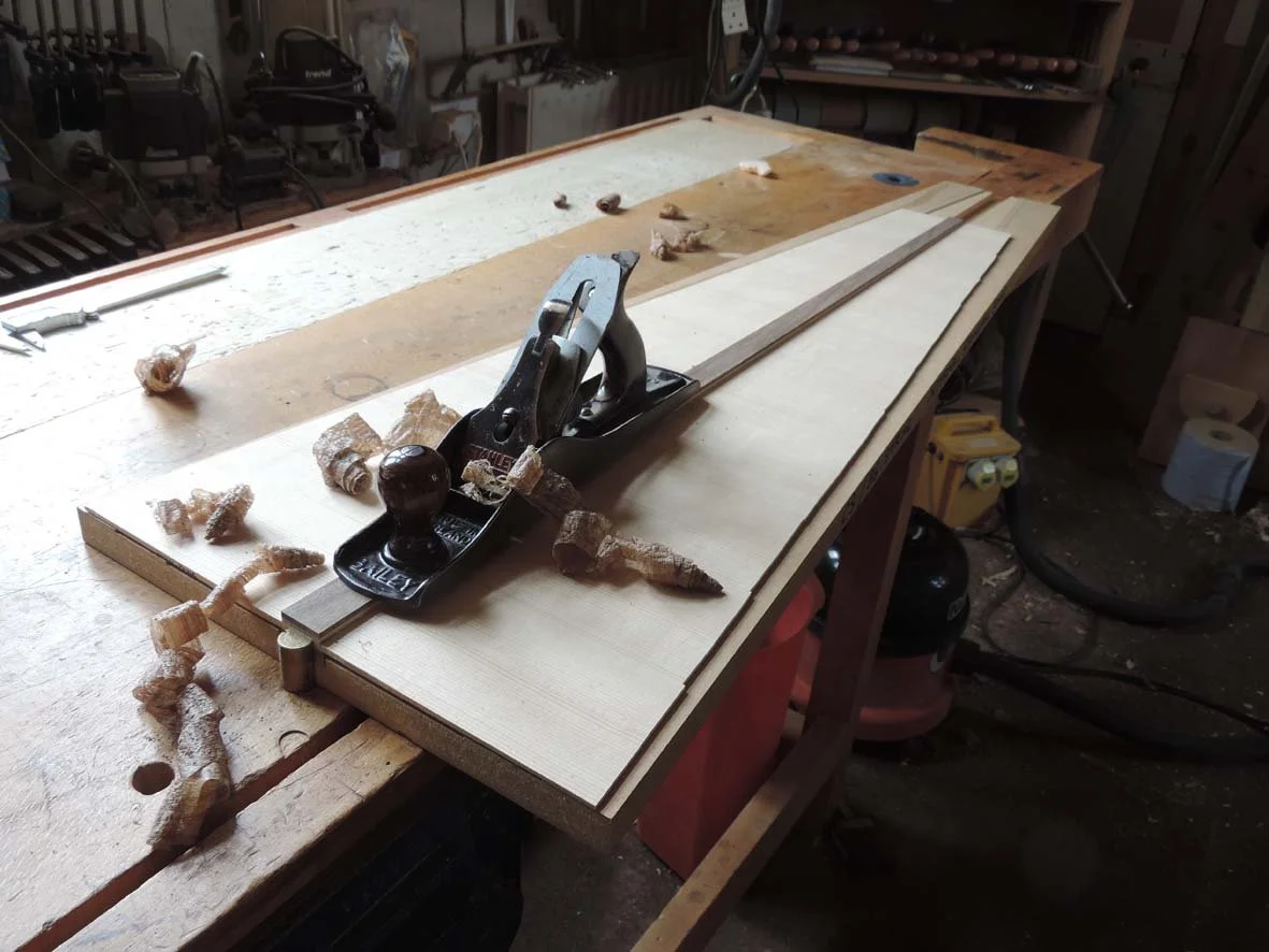 A woodworking workbench with a hand plane tool and shavings scattered around in a workshop.