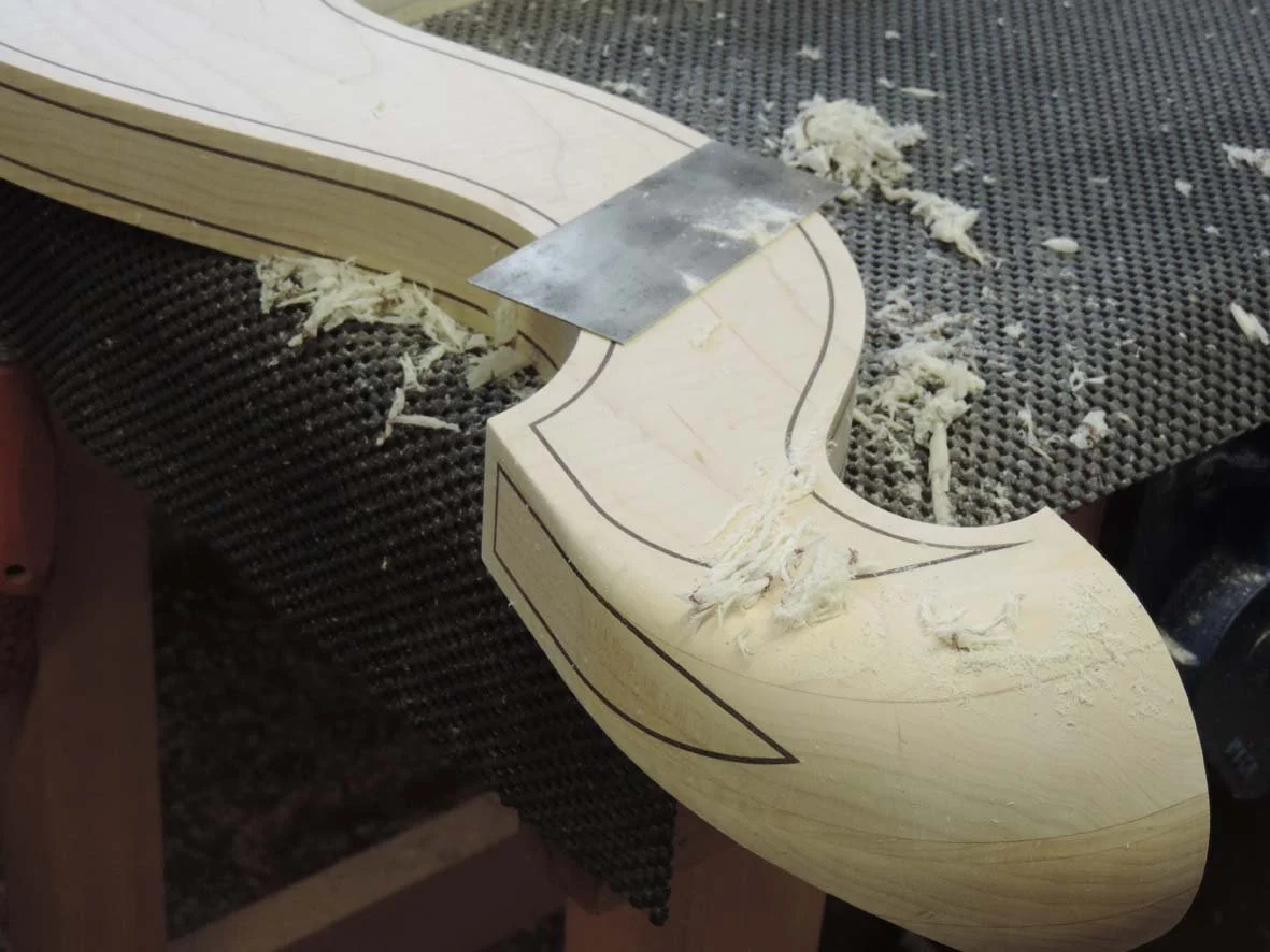 A harp-making project in progress with a wooden piece clamped to a work surface, sawdust, and shavings on the surface.