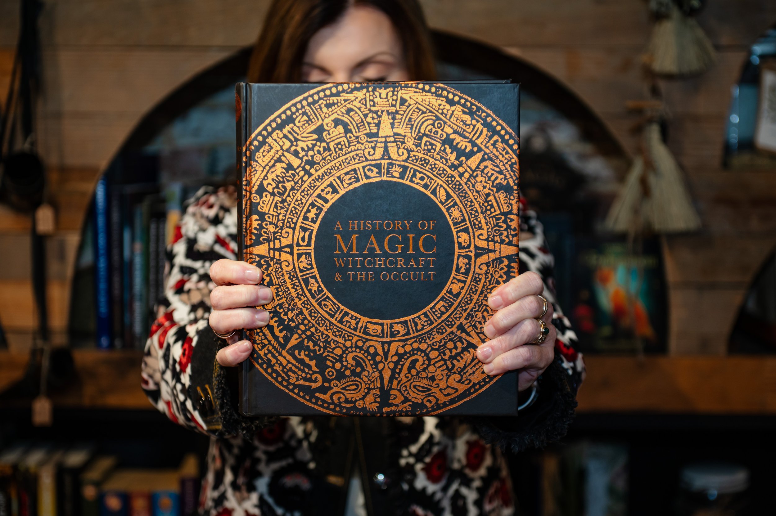 Woman holding a book up close with black and intricate gold art called "A History of Magic, Witchcraft, and the Occult".