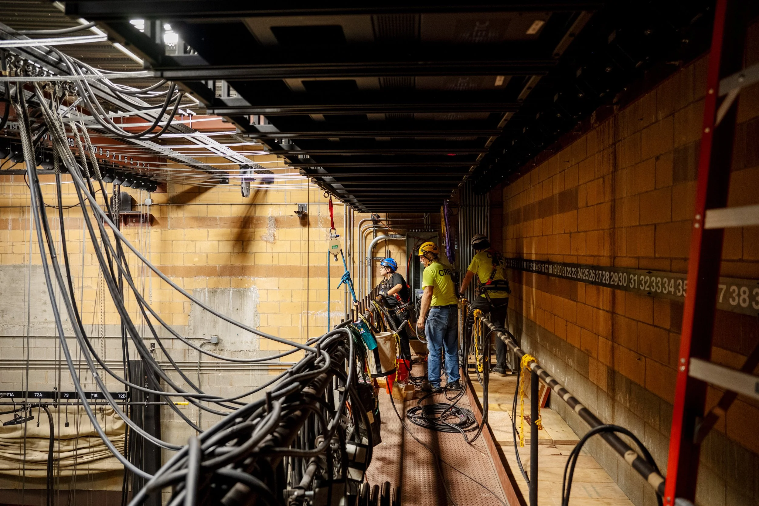 A group of wind turbine maintenance workers with safety helmets and harnesses working on a wind turbine nacelle, surrounded by cables and equipment.