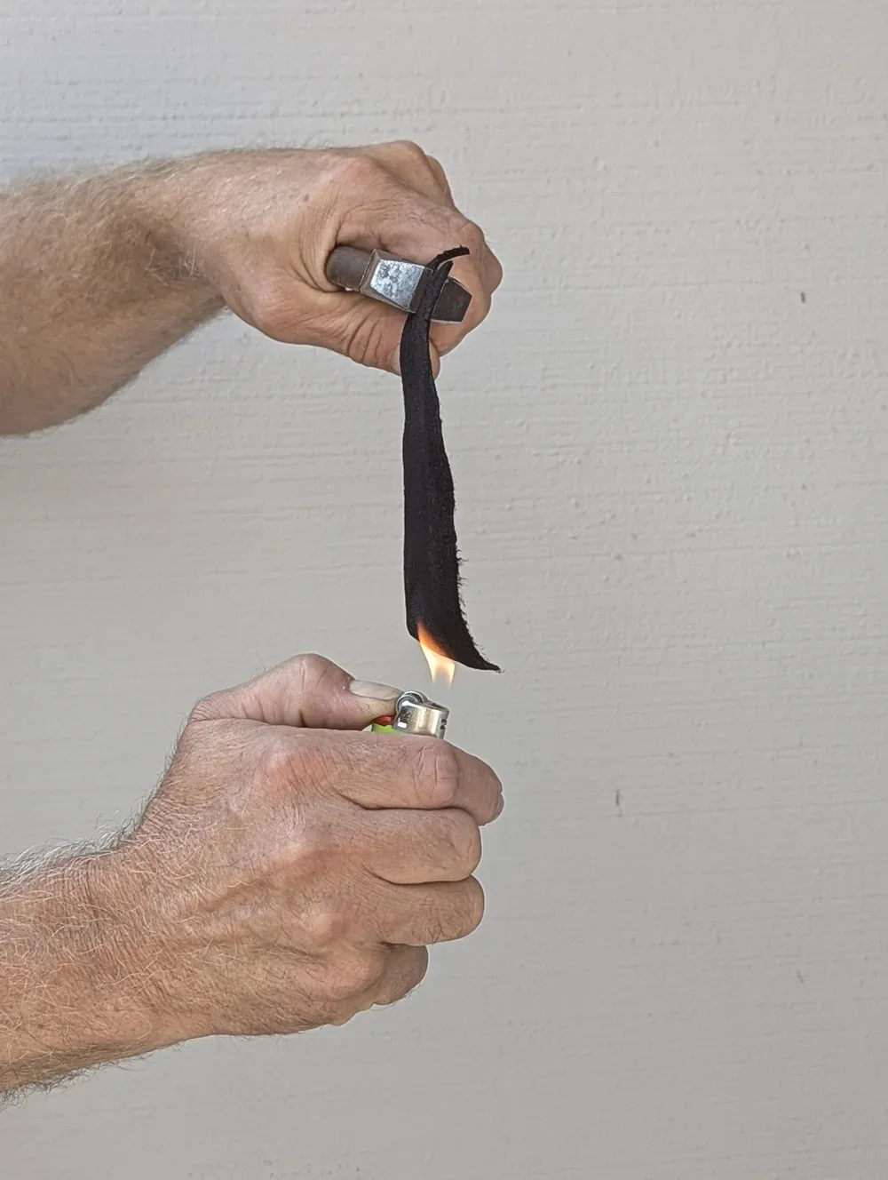 Person holding a lighter and igniting a matchstick wrapped in a black cloth, with a small flame at the tip.