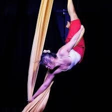An aerial silk acrobat performing a pose while hanging upside down from pink silk fabric.