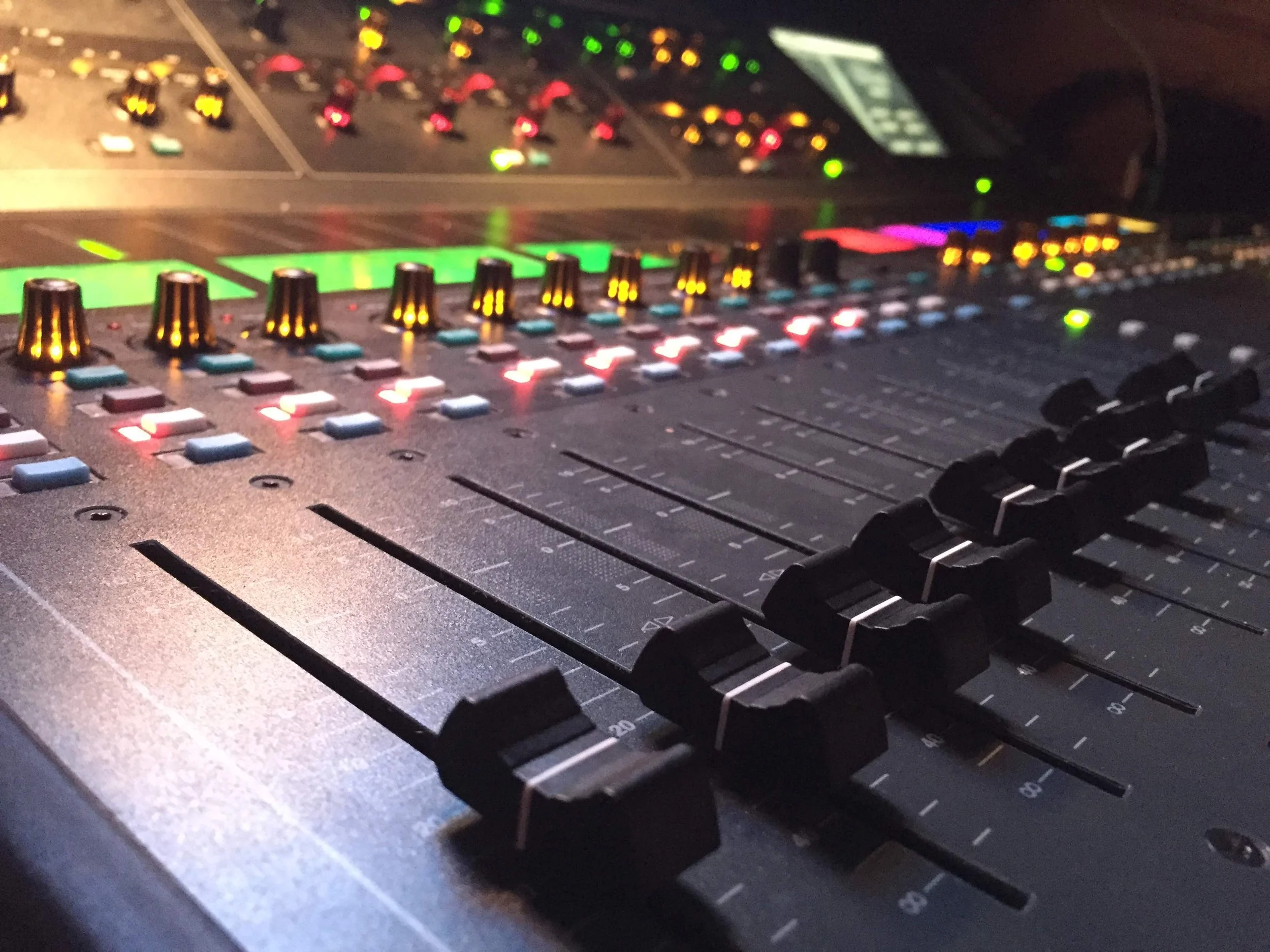 Close-up of a professional audio mixing console with illuminated colorful controls and faders.