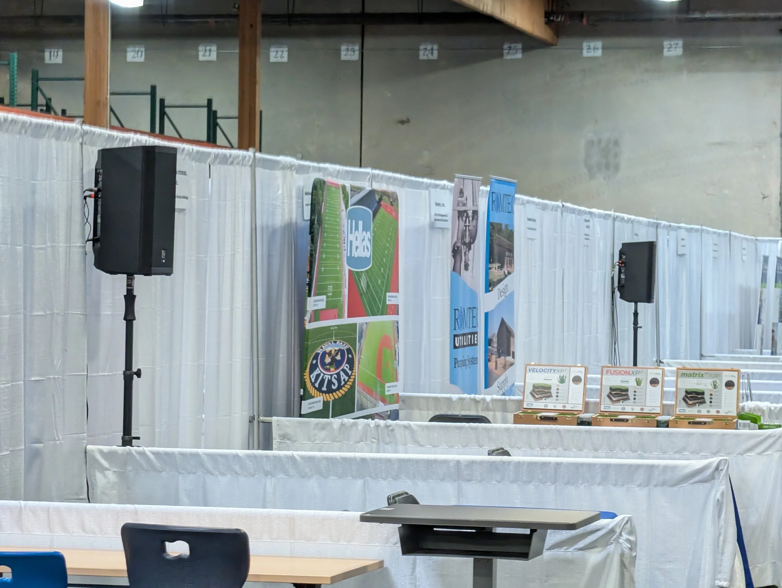 Empty indoor space with display boards and banners, set up for an event or exhibition, with tables and chairs visible.