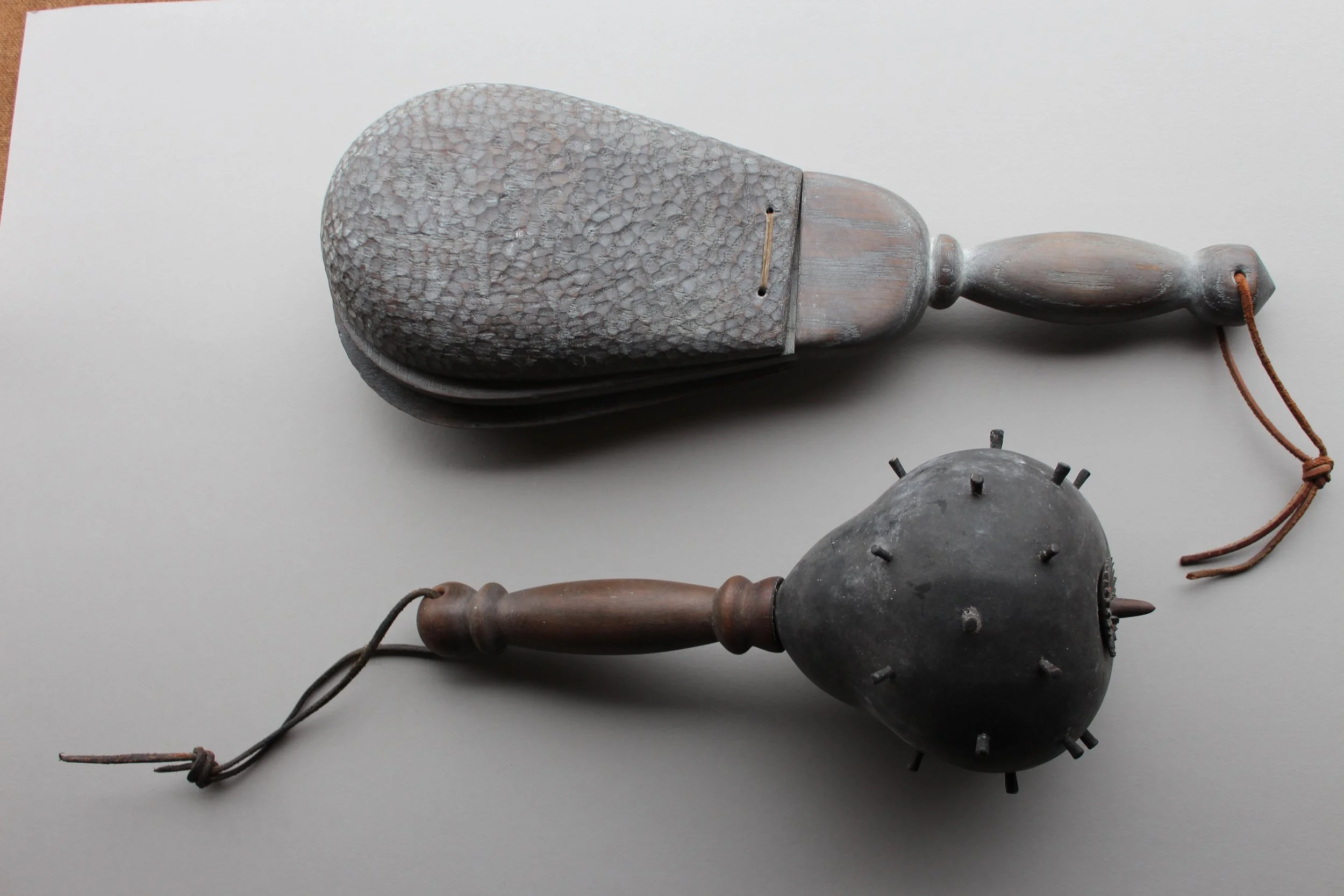 Two antique wooden tools with handles, one resembling a foot massager and the other a spiked rolling pin, placed on a white surface.