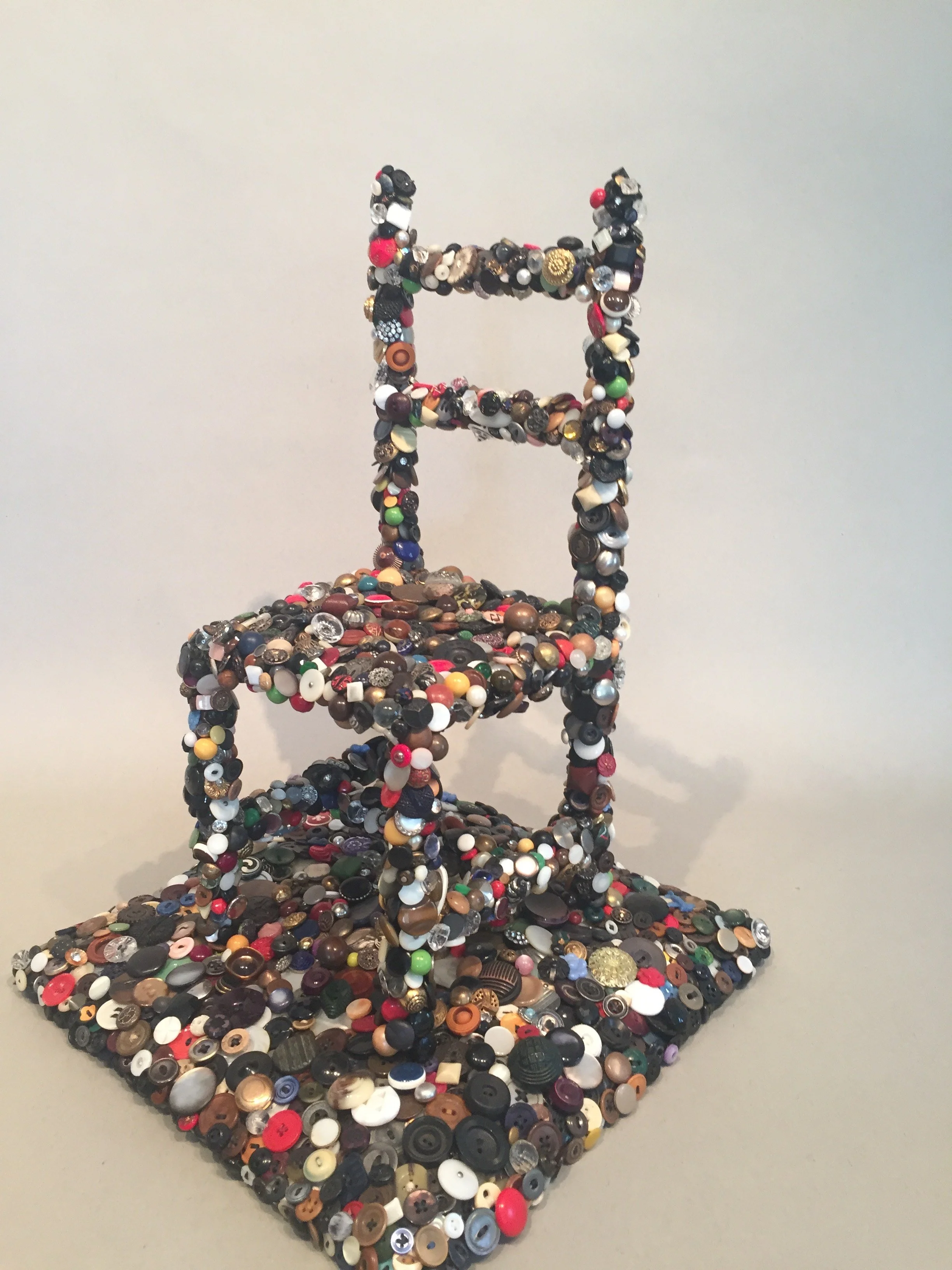 A chair sculpture made of numerous buttons covered in a variety of colors and sizes.