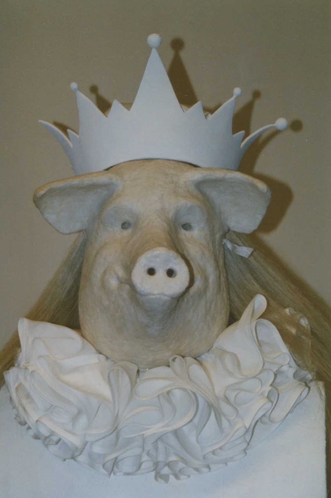 A pig sculpture wearing a paper crown and a ruffled collar.