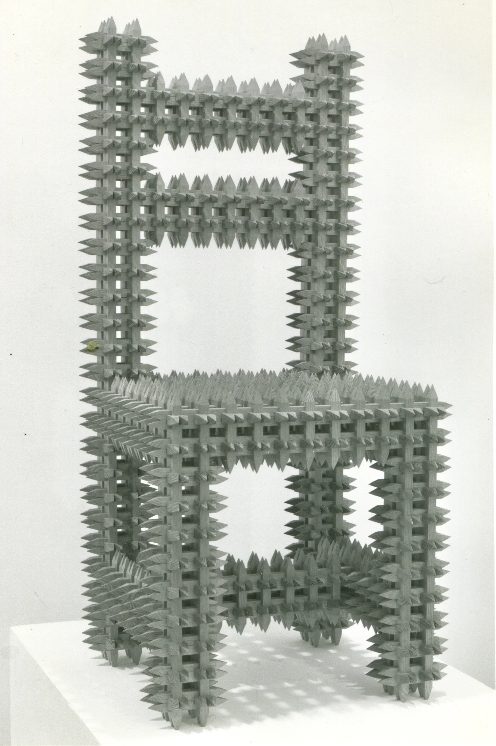 A large, abstract sculpture resembling a computer keyboard keycap structure, with sharp, pointed, interlocking elements creating a frame with multiple open spaces, displayed on a pedestal against a plain white background.