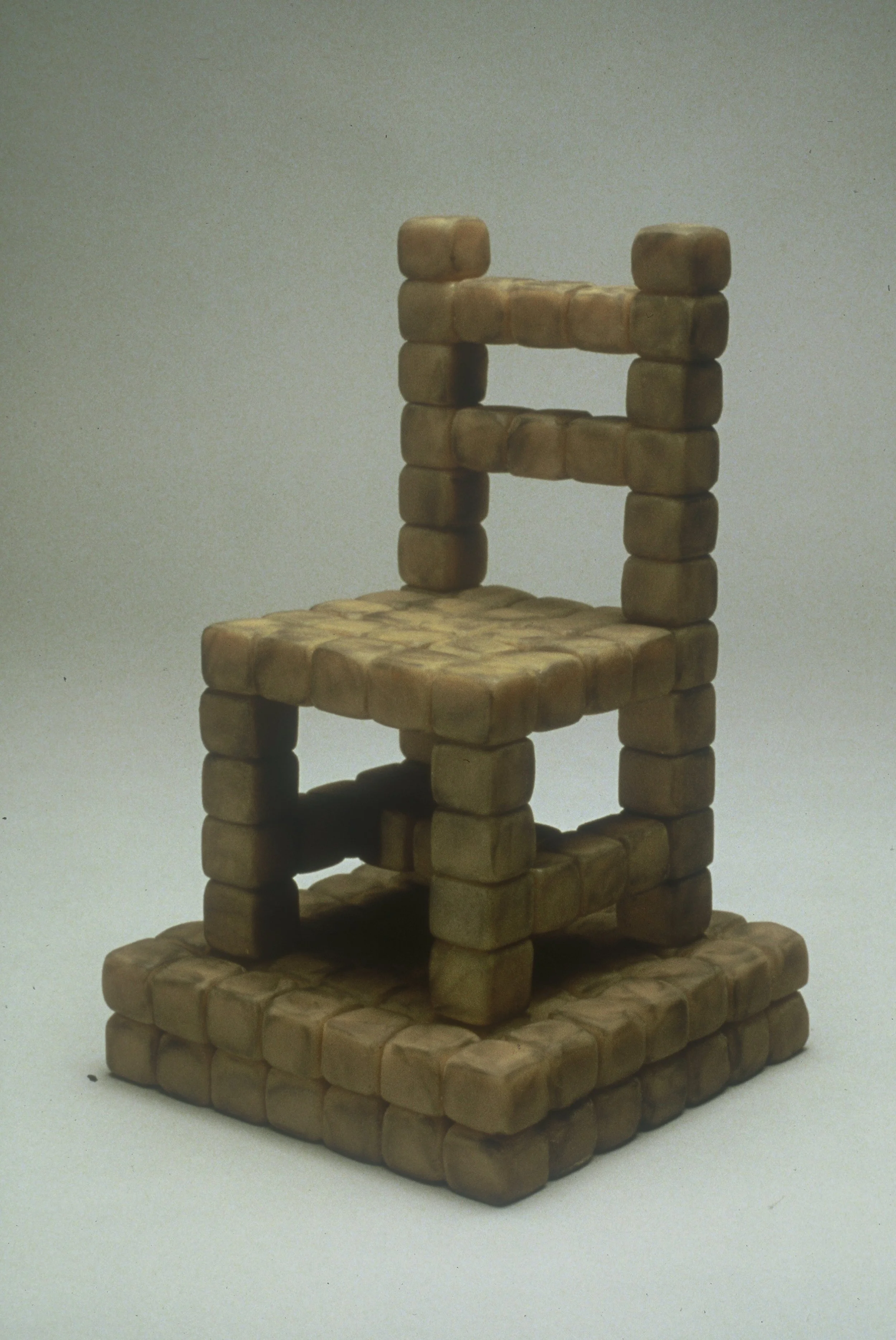 A small, tiered structure made of tiny, square, beige-colored blocks arranged in a staircase fashion against a plain background.