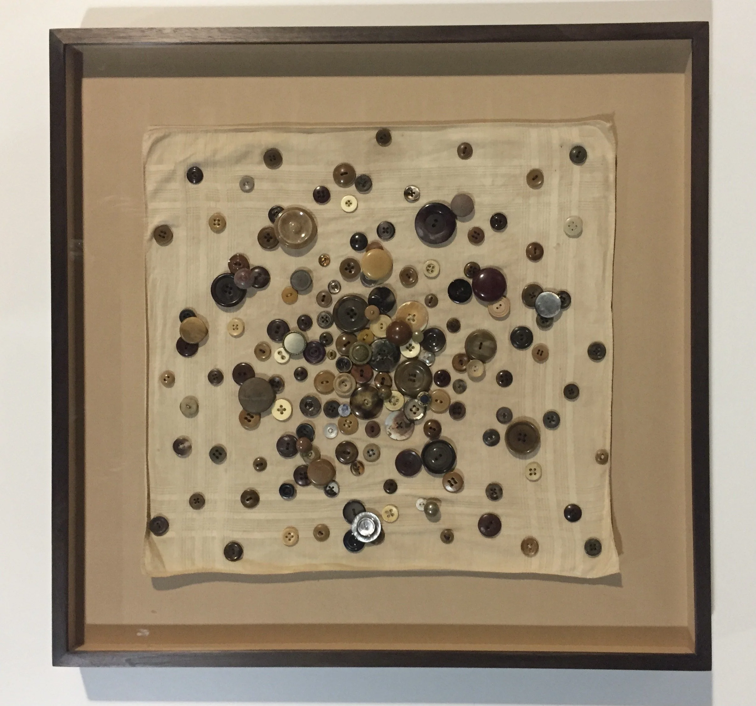 Framed display of scattered buttons in various sizes and colors on a fabric background.